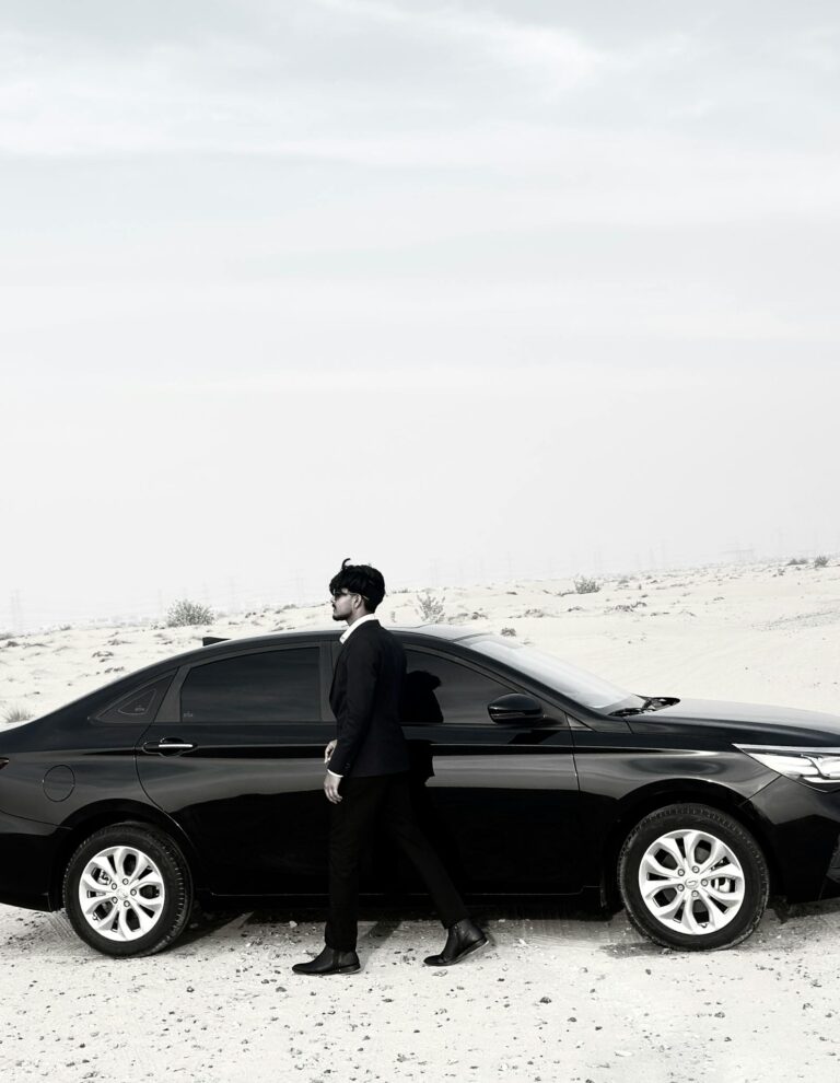 Elegant man in suit walking beside a black car in a desert landscape.