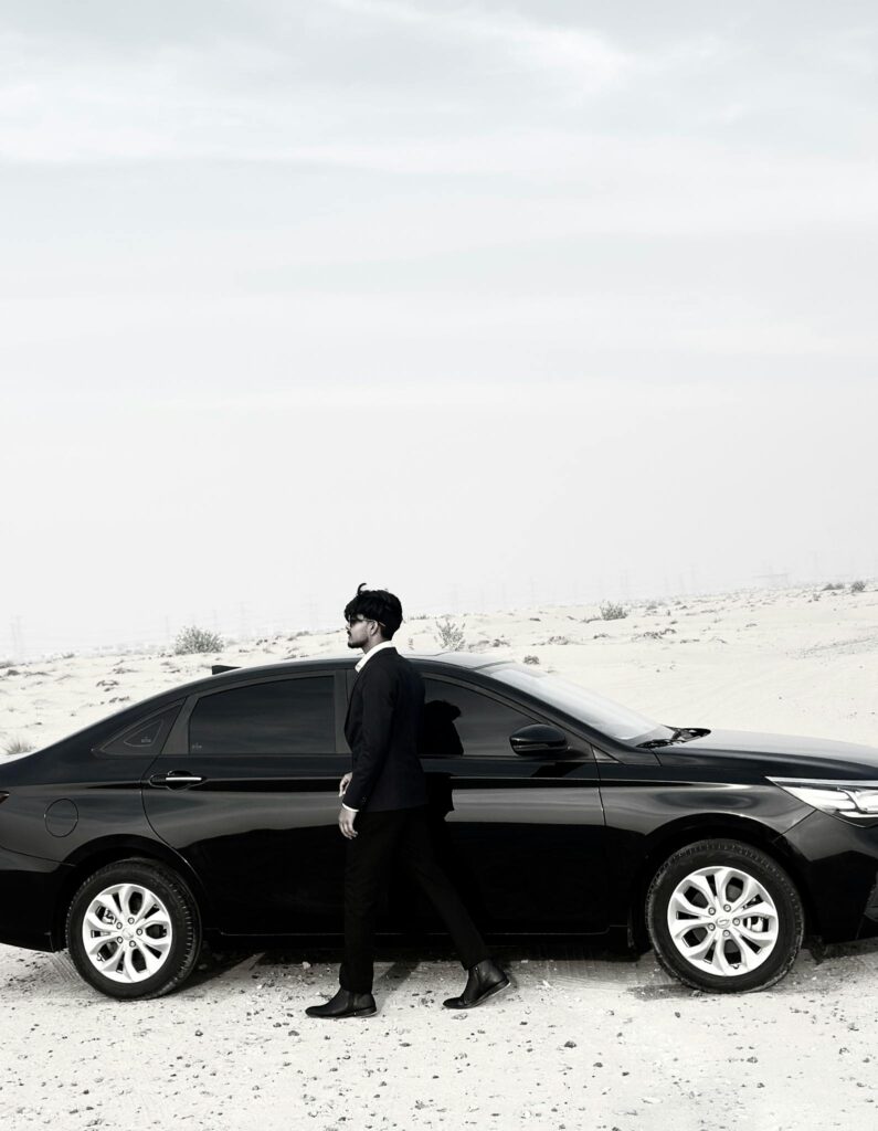 Elegant man in suit walking beside a black car in a desert landscape.